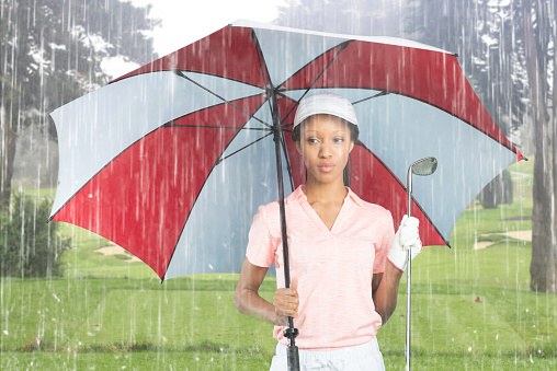 Women golfer on the golf course on a rainy day with an umbrella.