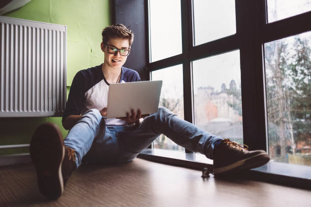 istock Student working with laptop sits on the floor near the window 939356142