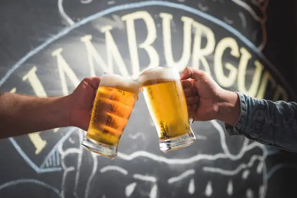 Two people toasting with chopp mugs with burger written background