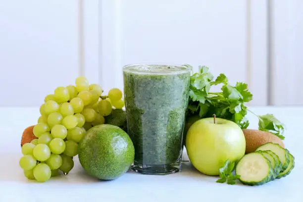 Green diet concept - number of green fruits and vegetables with green smoothie on a white table