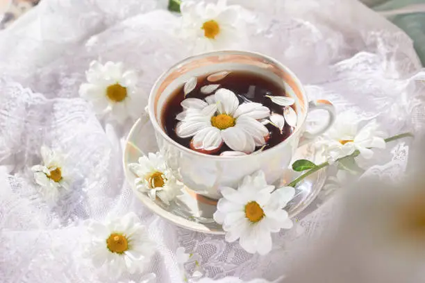 a cup of tea with chamomile on a table with a white tablecloth and flowers