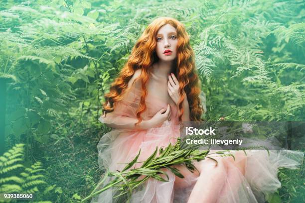 Beautiful Preraphaelite Girl With Curly Red Hair With A Flying Tulle Dress On The Background Of A Green Fern Stock Photo - Download Image Now