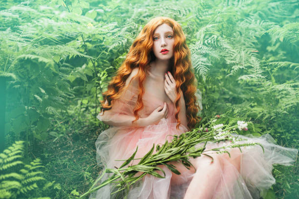 vestido de pre-raphaelite linda garota com cabelo vermelho encaracolado com um tule voando no fundo de uma samambaia verde - princess women duchesses renaissance - fotografias e filmes do acervo