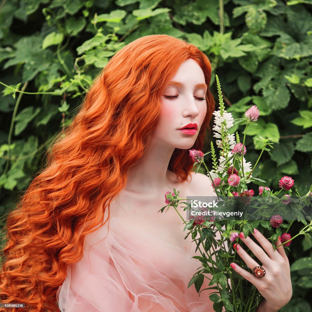 Beautiful pre-raphaelite girl with curly red hair with a flying tulle dress on the background of a fern Pre-Raphaelite Stock Photo