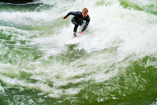 Silhouette of river surfer challenges raging green and white rapids on Eisbach River in middle of European city September 11, 2017 Munich Germany
