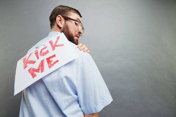 Amazed handsome businessman with beard wearing nerd glasses surprised with prank and taking out paper with Kick Me inscription from back