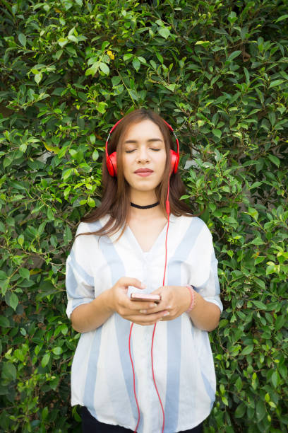 garota legal bonita moda ouvindo música em fones de ouvido vermelhos sobre fundo de arbustos. - arab style audio - fotografias e filmes do acervo