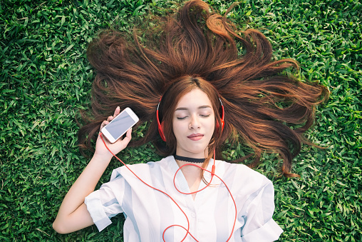 Indian girl listening to music streaming with headphones from smartphone in summer on a meadow.
