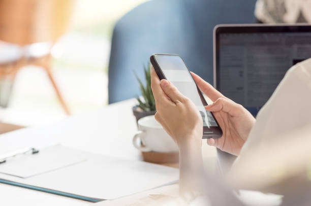 weibliche hand mit smartphone während der arbeit am schreibtisch im büro - businesswoman using computer computer monitor women stock-fotos und bilder