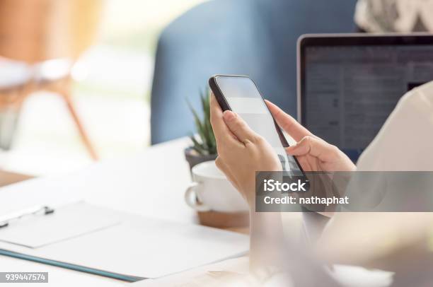 Female Hand Using Smartphone While Working At Desk In Office Stock Photo - Download Image Now