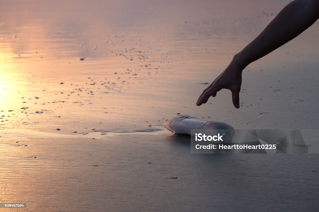 The hand of a woman is picking up a plastic bottle The hand of a woman is picking up a plastic bottle to clean the beach. Beach Stock Photo