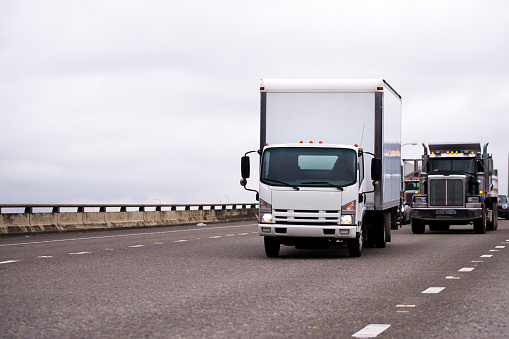 Small semi truck fleet with box trailer and big rig classic semi truck fleet running on wide highway with traffic left behind