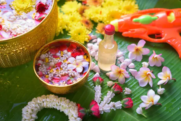 Photo of Thai traditional jasmine garland and Colorful flower in water bowls decorating and scented water, perfume, marly limestone, pipe gun on Banana leaf for Songkran Festival or Thai New Year