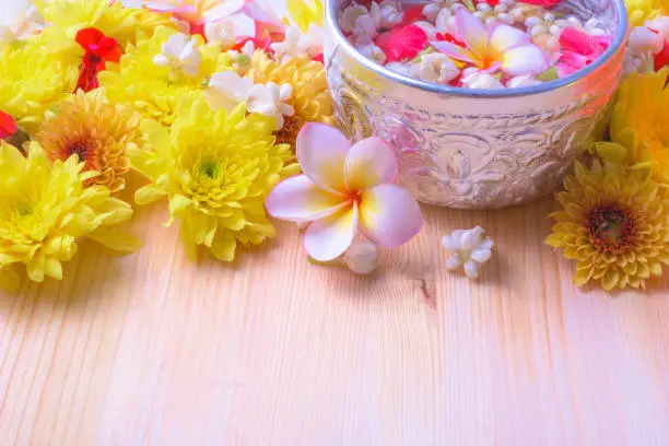 Photo of Thai traditional jasmine garland and Colorful flower in water bowls decorating and scented water, perfume, marly limestone, pipe gun on wood background for Songkran Festival or Thai New Year