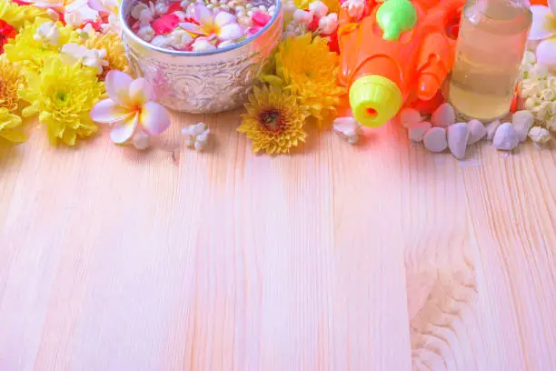 Photo of Thai traditional jasmine garland and Colorful flower in water bowls decorating and scented water, perfume, marly limestone, pipe gun on wood background for Songkran Festival or Thai New Year