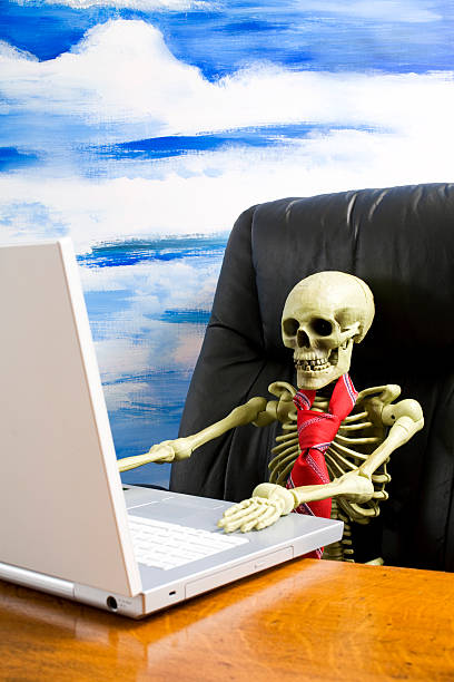 Skeleton wearing tie in executive chair with laptop on desk