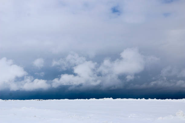 istock snow field. The plain is covered with white snow under a blue sky with thick white clouds. before a snowfall, a storm, a snowstorm. premonition of a blizzard. in anticipation of a blizzard. 939493980