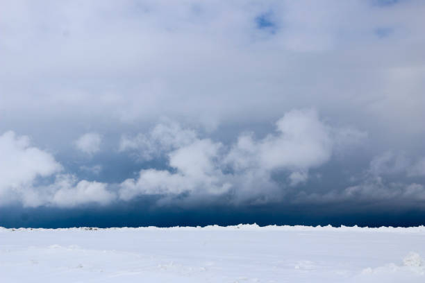 istock snow field. The plain is covered with white snow under a blue sky with thick white clouds. before a snowfall, a storm, a snowstorm. premonition of a blizzard. in anticipation of a blizzard. 939494006