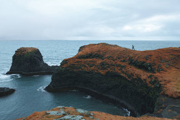 istock man walking on cliff at beautiful ocean, Arnarstapi, iceland 939494286