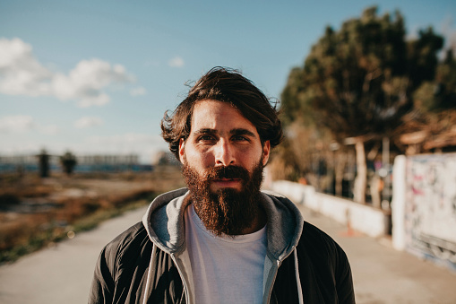 Young man with with long beard walking and posing in the city suburbs with casual style clothes.