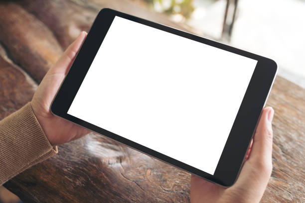 istock Mockup image of hands holding black tablet pc with blank white desktop screen on wooden table 939514040