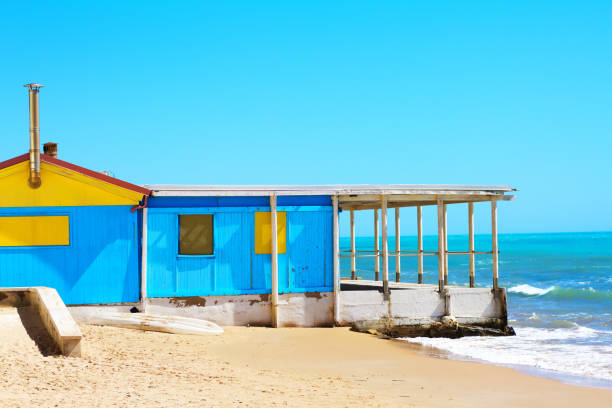 Punta Secca (Ragusa), Sicily: A pretty blue and yellow wooden kiosk/restaurant sits on a winter beach in the fishing village of Punta Secca, a fishing village in Ragusa Province. The kiosk is closed and boarded up.