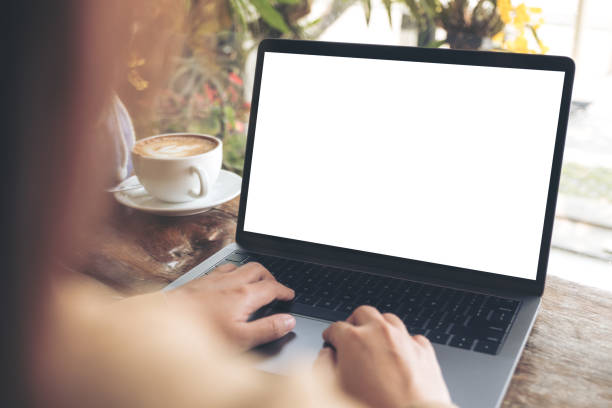 istock Mockup image of woman's hands using and typing on laptop with blank white desktop screen on wooden table in cafe 939514234