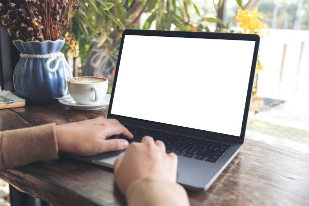 istock Mockup image of woman's hands using and typing on laptop with blank white desktop screen on wooden table in cafe 939514424