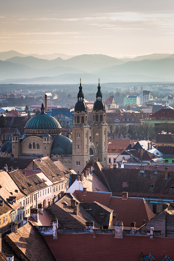 Horizontal color image depicting the ancient, medieval skyline of Sibiu, a city in the Transylvania region of Romania. In the foreground we can see two orthodox church spires, while beyond we can see traditional Germanic architecture of the town's buildings and houses spread out. In the distance the snow-capped Carpathian mountains provide a beautiful backdrop on this winter Decemver day. Room for copy space.