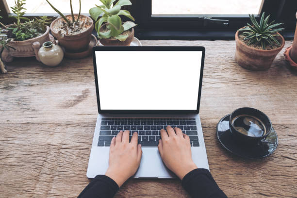 istock Top view mockup image of hands using and typing on laptop with blank white desktop screen with coffee cup on vintage wooden table in cafe 939515826