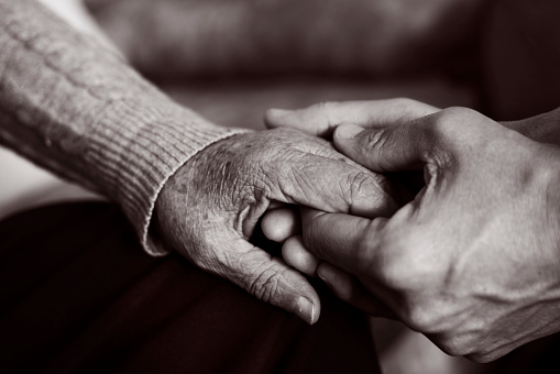 closeup of a young caucasian man holding the hand of an old caucasian woman with affection, in black and white