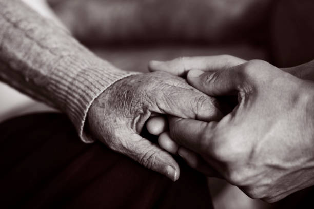 young man holding the hand of an old woman closeup of a young caucasian man holding the hand of an old caucasian woman with affection, in black and white alzheimers disease photos stock pictures, royalty-free photos & images