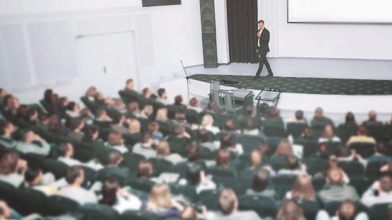 Speaker at a business convention and presentations. The audience on the large number of people. The announcer with a microphone in his hands