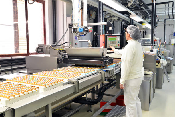 プラリネ食品産業 - チョコレートとコンベア ベルトの労働者のための工場での生産 ストックフォト