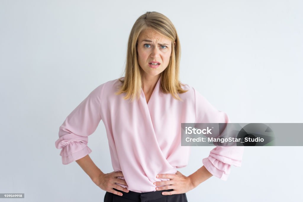 Portrait of displeased young businesswoman Portrait of young Caucasian businesswoman wearing pink blouse standing with hands on waist displeased at some rude behavior. Irritation, misunderstanding concept Women Stock Photo