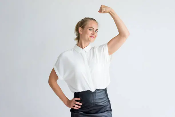 Portrait of positive young Caucasian woman wearing white shirt showing bicep. I can do it concept