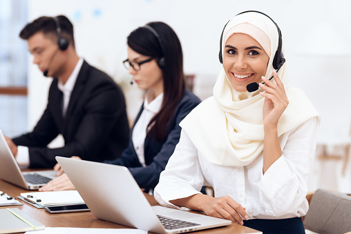 An Arab woman works in a call center. She's an operator. Her colleagues work nearby.
