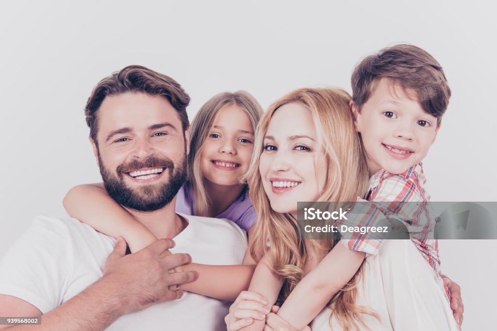 Family photo portrait. Four relatives are hugging on the white background, smiling, at home, blond mum is piggy backing the cute small son Family Stock Photo