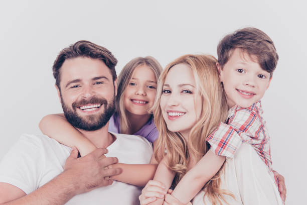 Family photo portrait. Four relatives are hugging on the white background, smiling, at home, blond mum is piggy backing the cute small son Family photo portrait. Four relatives are hugging on the white background, smiling, at home, blond mum is piggy backing the cute small son honeymoon photos stock pictures, royalty-free photos & images