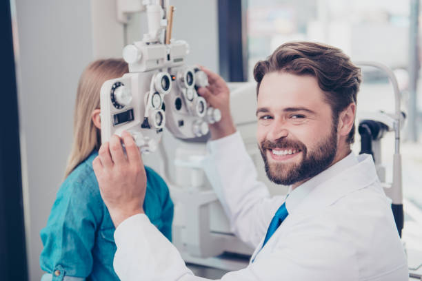 Close up of attractive cheerful brunet bearded optician, doing the eye sight check up for small blond girl at his office, smiling Close up of attractive cheerful brunet bearded optician, doing the eye sight check up for small blond girl at his office, smiling ophthalmologist photos stock pictures, royalty-free photos & images