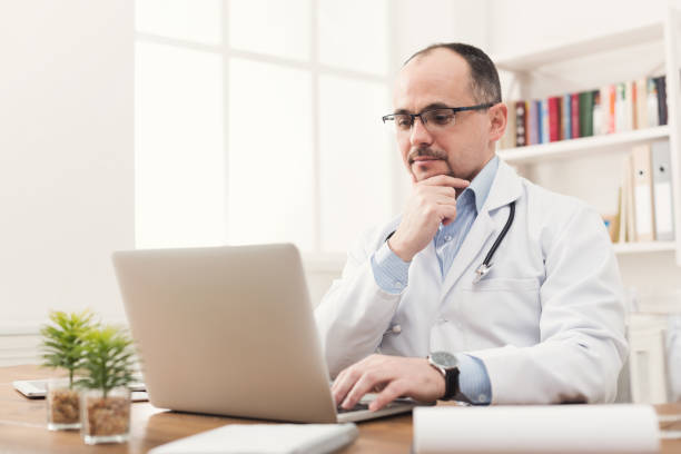 istock Serious doctor in glasses typing on laptop 939578612