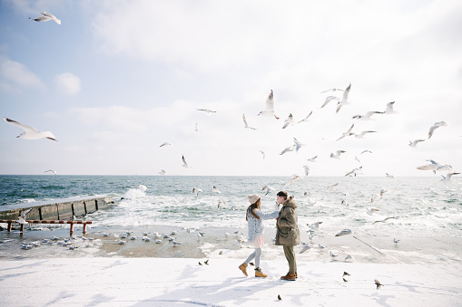happy young couple walking on seashore with seagulls in winter