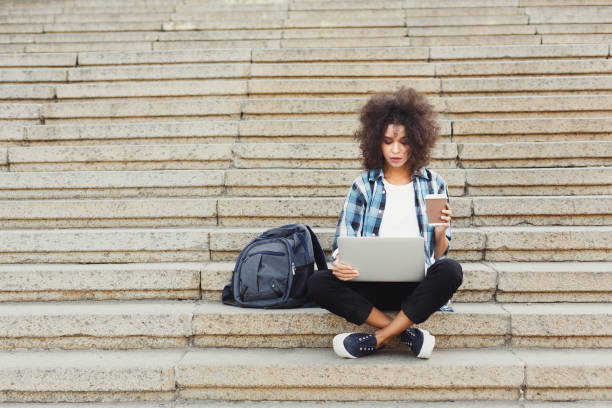 istock Pensive student sitting on stairs using laptop 939586354