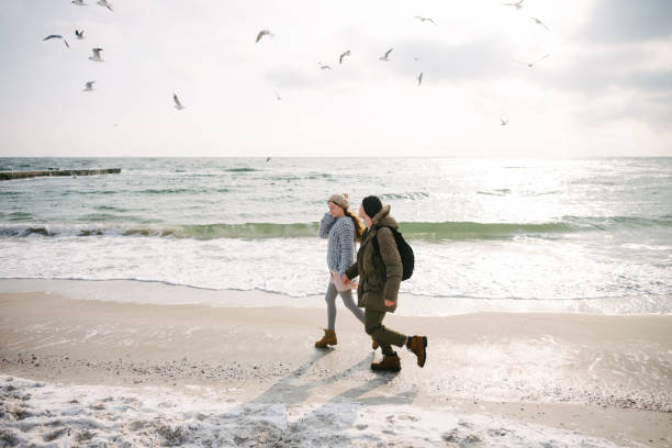 istock young couple holding hands and running on winter seashore with seagulls 939586686