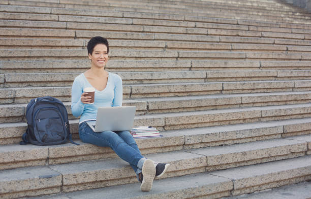 istock Female student working on a laptop and drinking coffee outside 939597602