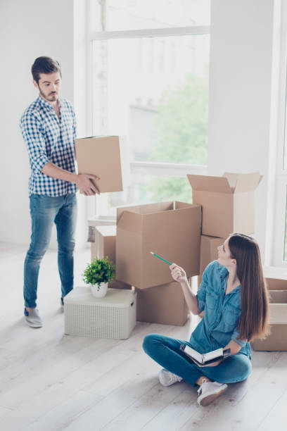 home, sweet home! young cute couple is packing to move to their new accomodation, girlfriend is writing a list not to forget nothing, both are in casual clothes - to do list organization life family imagens e fotografias de stock