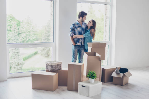 exitosa pareja joven se muda a nuevo lugar agradable y abrazar, son cajas de cartón con sus pertenencias. la habitación es muy ligera y brillante, que están usando ropa casual - common family new togetherness fotografías e imágenes de stock