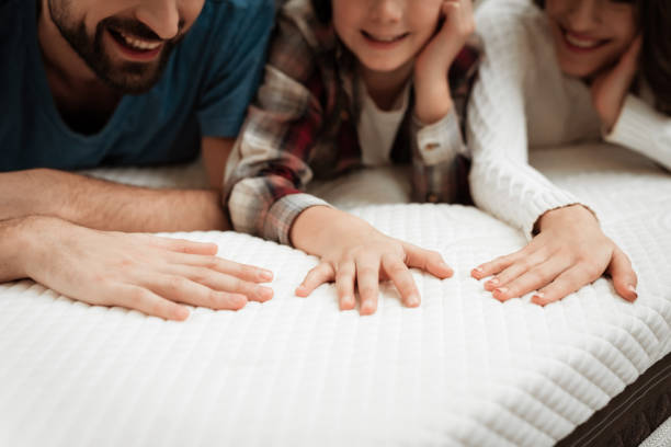 Young couple together with their young son test material of mattress for a touch. Young couple together with their young son test the material of the mattress for a touch. Family buys mattress in furniture store. Healthy posture concept. mattress stock pictures, royalty-free photos & images