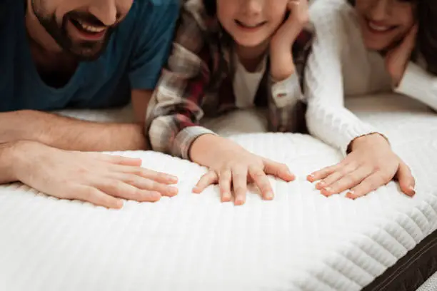 Young couple together with their young son test the material of the mattress for a touch. Family buys mattress in furniture store. Healthy posture concept.
