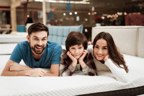 Lovely bearded man, together with his beautiful wife and son, relaxes on the mattress in the store. stock photo